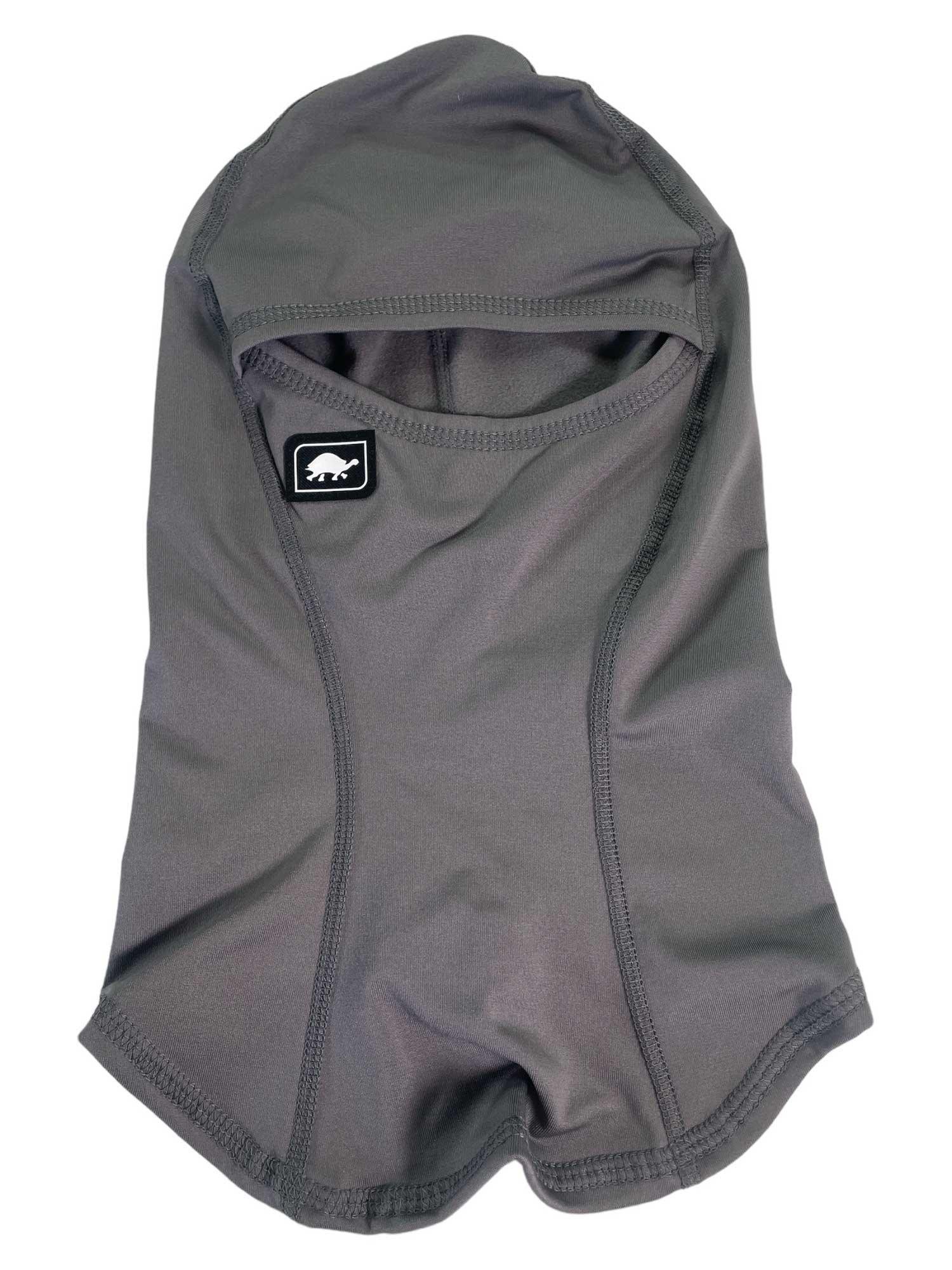 The Turtle Fur Comfort Shell Ninja Balaclava is gray, made from smooth, stretchy fabric with visible stitching and features a small bear logo patch on the left side near the face opening.
