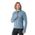 A smiling person with long, wavy hair zips up a light blue Smartwool Men's Smartloft Jacket, made with recycled wool insulation, paired with black athletic pants and standing against a plain white background.