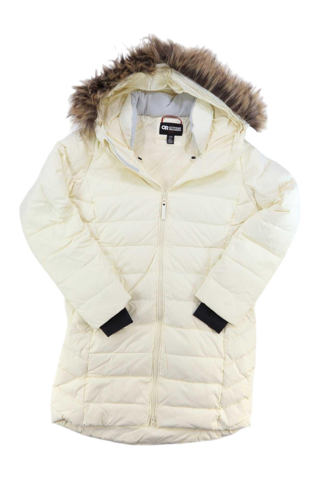 The Outdoor Research Women's Coze Faux Fur Parka is a long off-white down jacket with a zip front, black inner cuffs, and a brown faux fur-trimmed hood. Shown laid flat with crossed sleeves for a cozy look; made from recycled nylon.