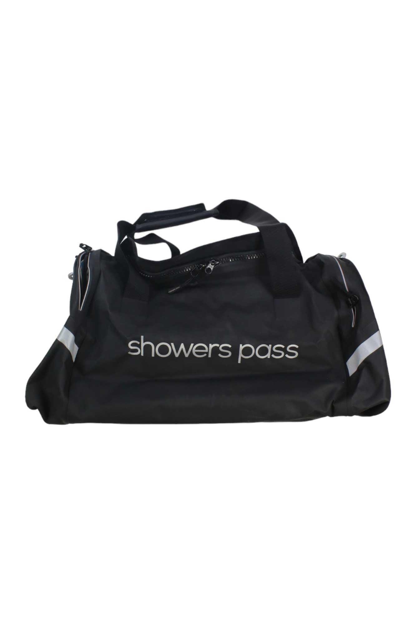 The Showers Pass Waterproof Duffel Bag is black with white branding, made of ballistic nylon. It features a zipper closure, two handles, and reflective edge stripes—ideal for carrying cycling gear.