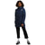 A person stands against a white background wearing The North Face Womens Gotham Parka in navy blue, made with recycled down and water-repellent fabric, featuring a hood, paired with black pants, white socks, and black-and-white sneakers.