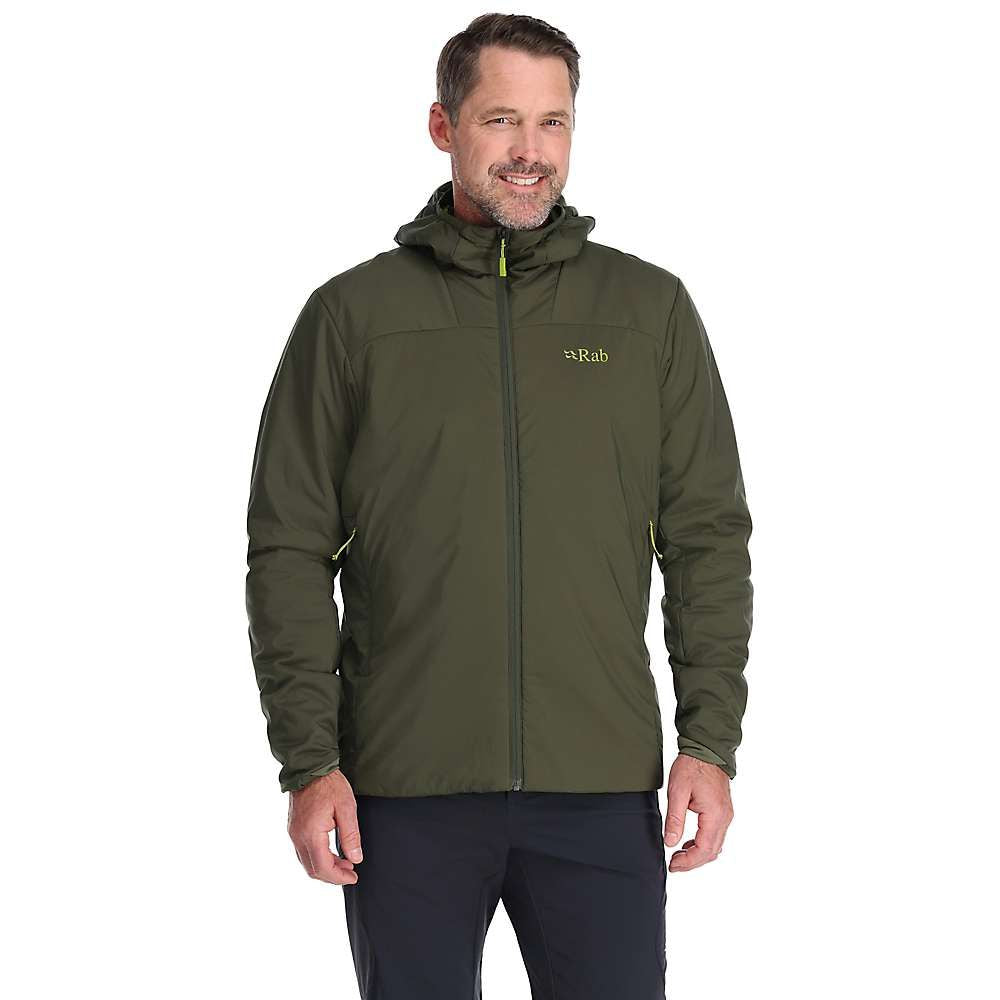 A man stands smiling with hands relaxed at his sides, wearing a dark green Rab Mens Xenair Alpine Light Jacket, against a plain white background.