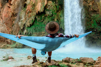 A man sitting on a hammock in front of a waterfall