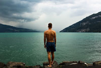 a man standing by lake in swim trunks