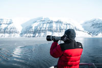 A man wearing a jacket photographing an iceberg