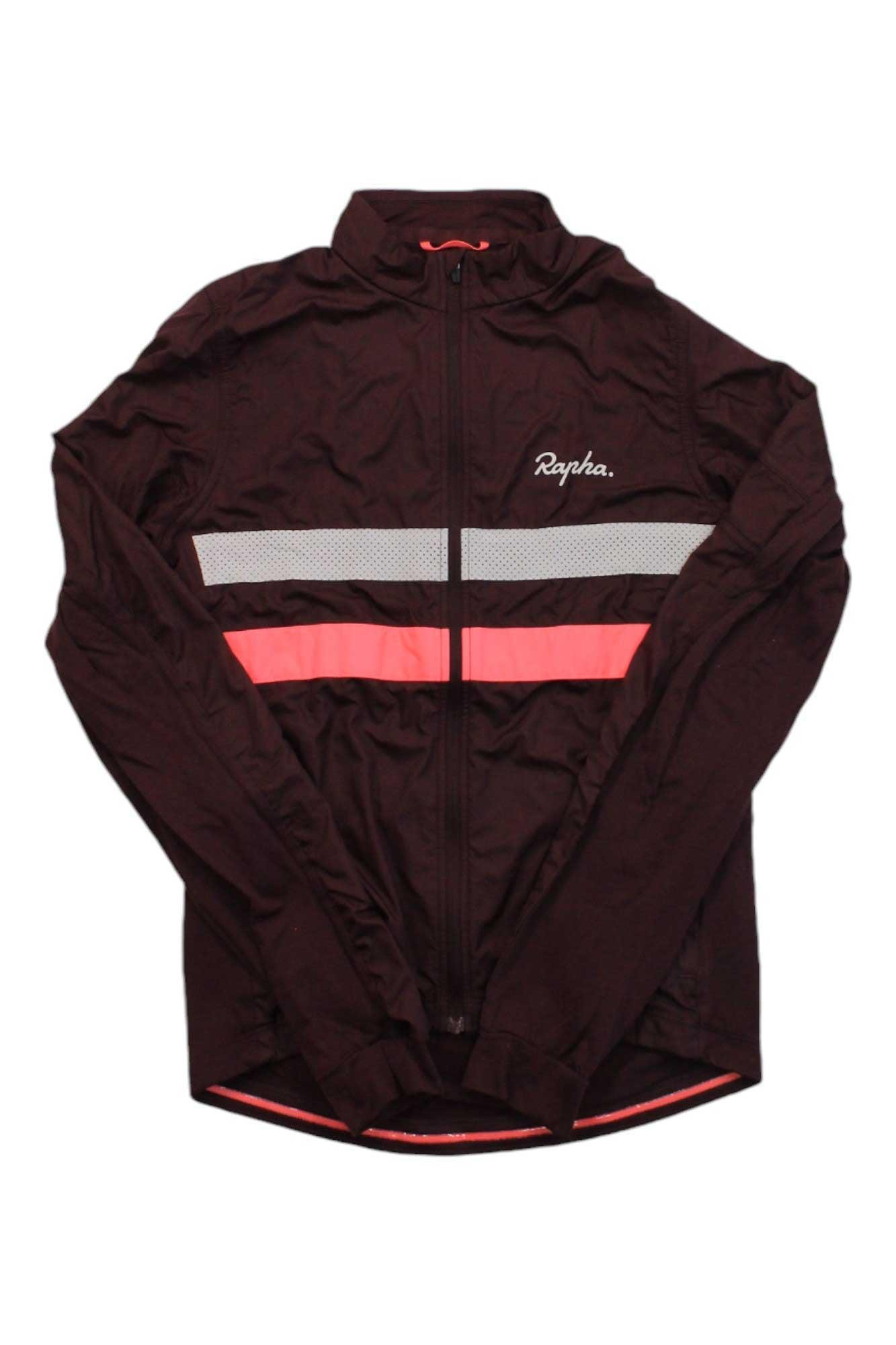 The Rapha Mens Brevet Long Sleeve Windblock Jersey is a black cycling jacket with a front zipper, white and pink chest stripes, and the "Rapha." logo on the left side.