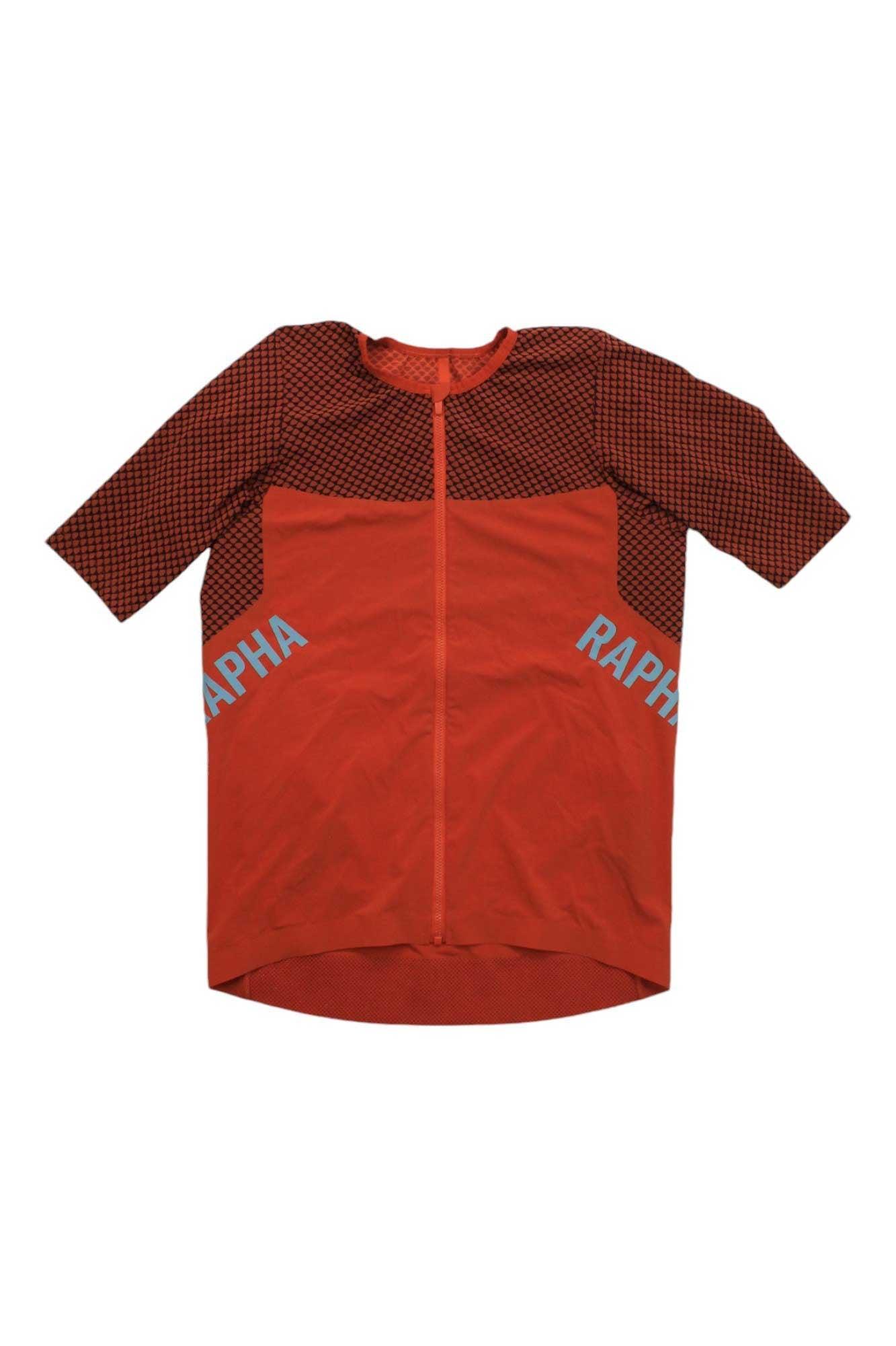 The Rapha Men’s Pro Team Crit Jersey features a red, short-sleeve aerodynamic design with a front zipper, black mesh on shoulders and sleeves, and RAPHA in light blue on both sides.
