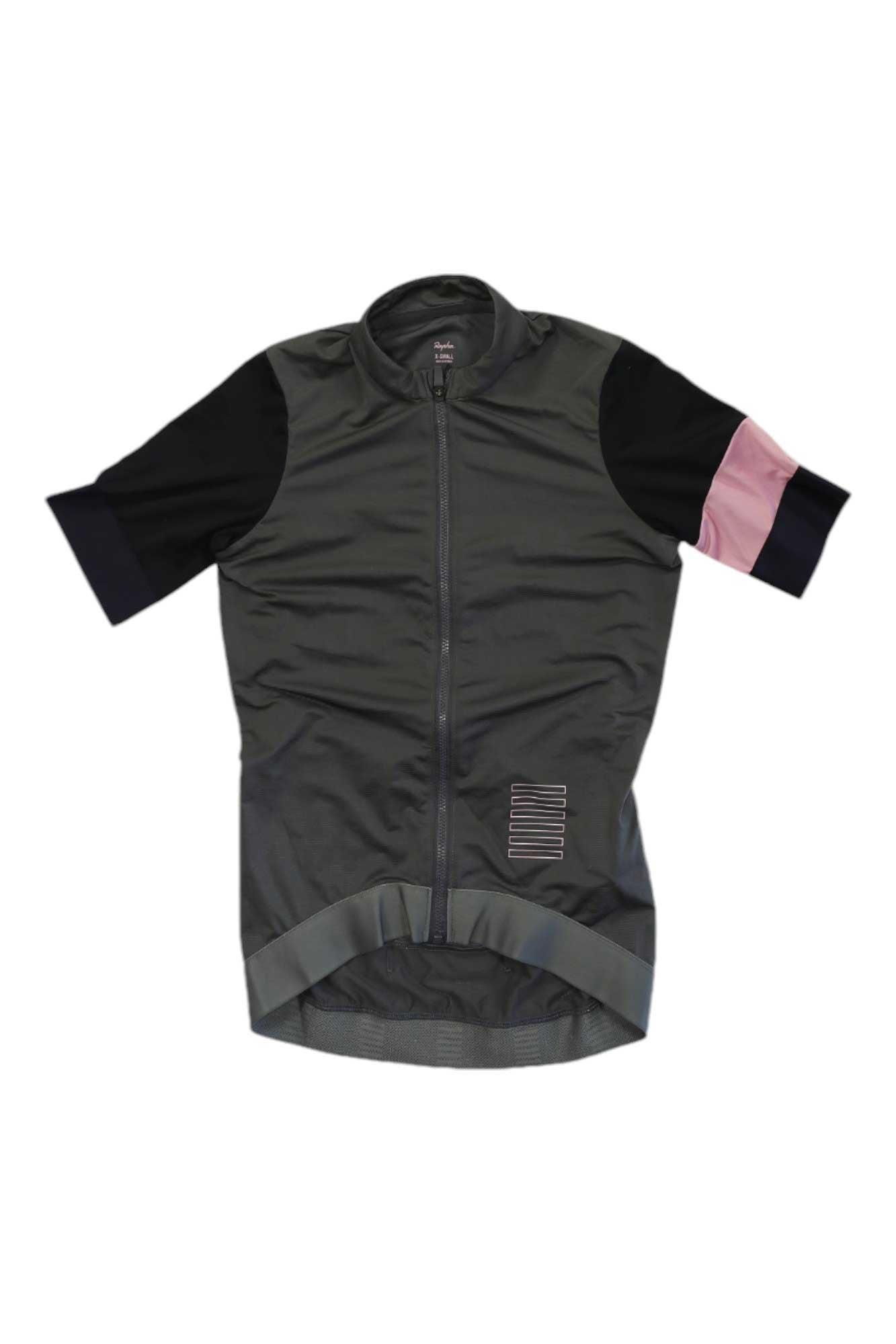 The Rapha Women's Pro Team Training Jersey is a short-sleeve dark gray cycling jersey with black sleeves, featuring pale pink and navy color blocks on the left sleeve, a front zipper, and a small rectangular patch near the hem.