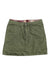 The Womens Prairie Dawn Skirt is an olive green mini skirt featuring front pockets, button and zipper closure, and plaid lining at the waistband. The fabric resembles cotton or a similar material.