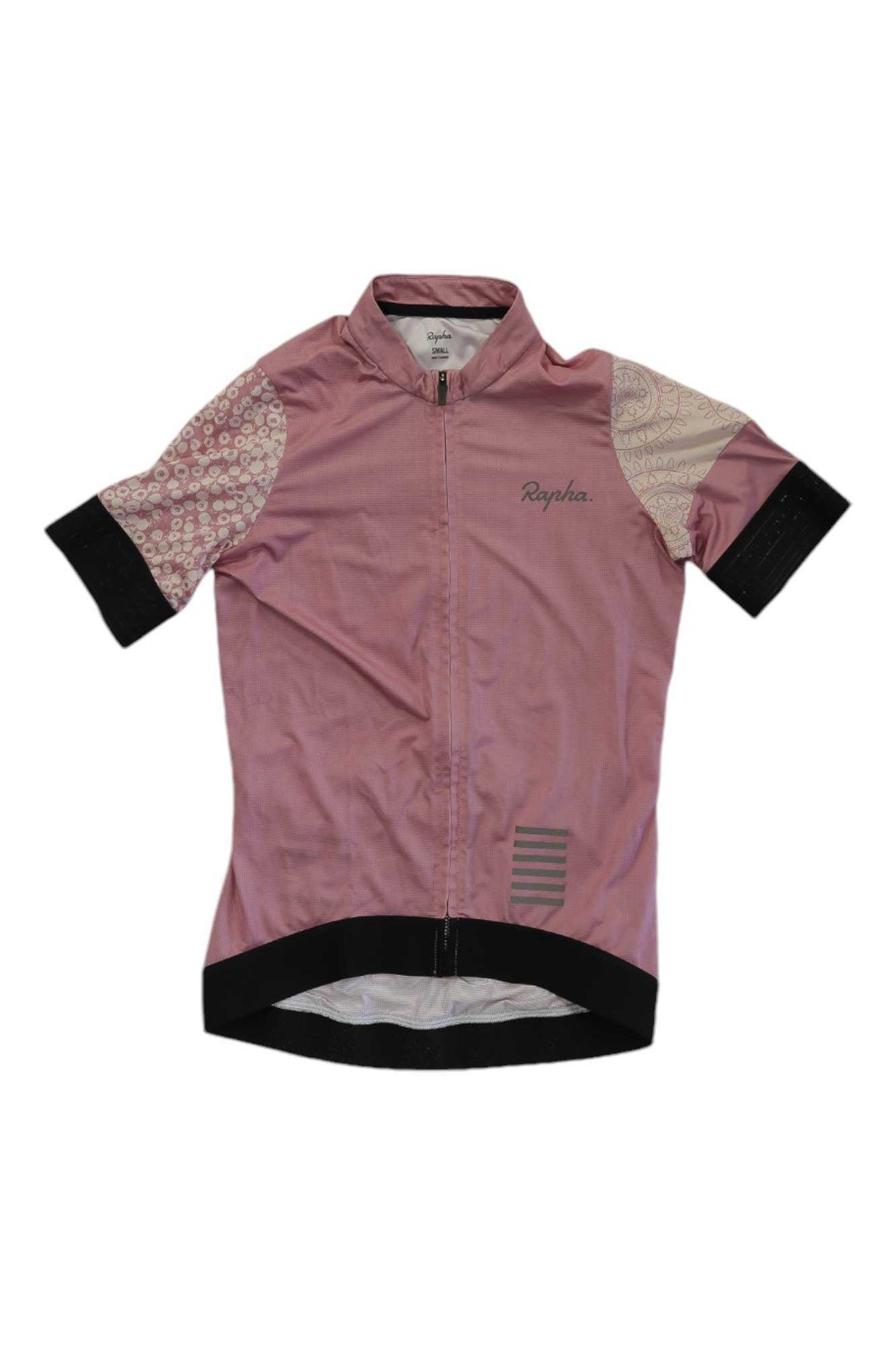 The Rapha Womens Pro Team Training Jersey is a light pink short-sleeve cycling jersey with patterned sleeves, black cuffs and hem, front zipper, and "Rapha" printed on the chest—a stylish and eco-friendly choice for cyclists.