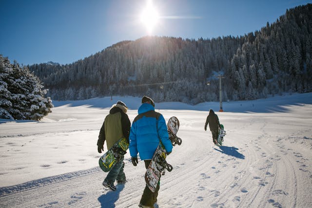 Three snowboarders walking across a trail