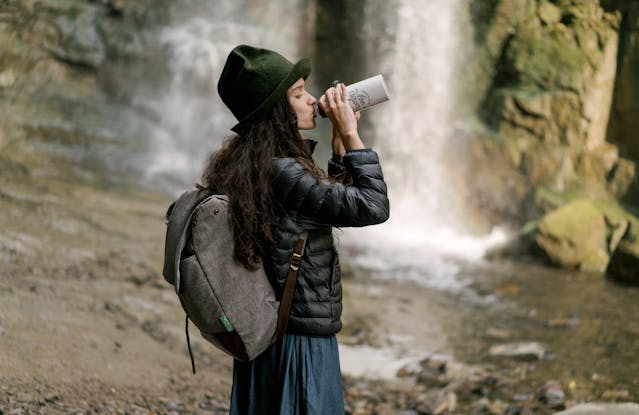 woman drinking from a water bottle next to a waterfall