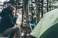 woman sitting by a tent with coffee