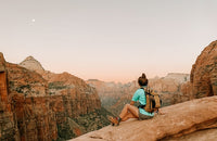 A woman sitting on a rock overlooking a canyon